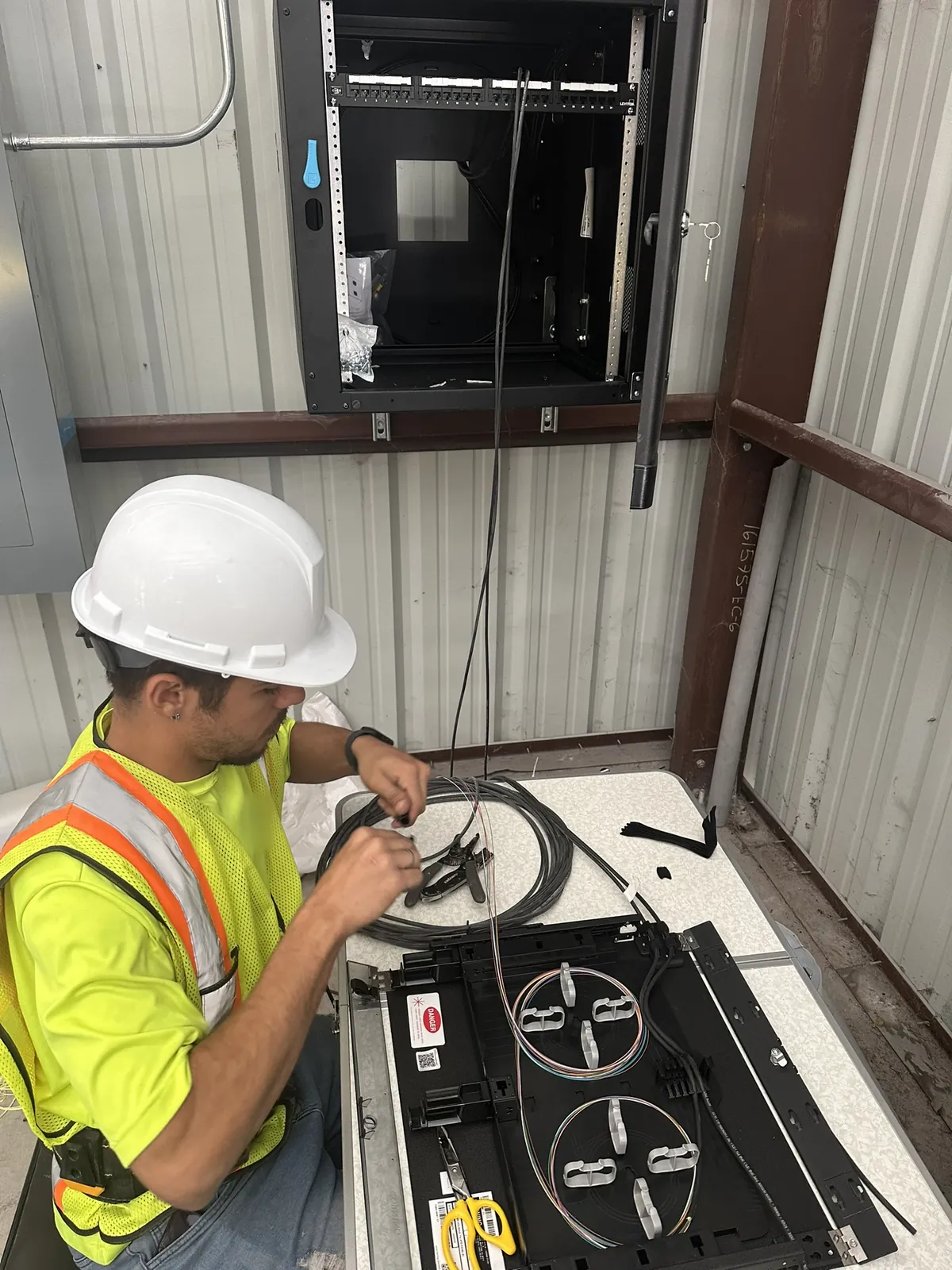 Fiber optic technician organizing fibers at a wall-mounted enclosure at a Data Pro Communications project in Orlando, FL