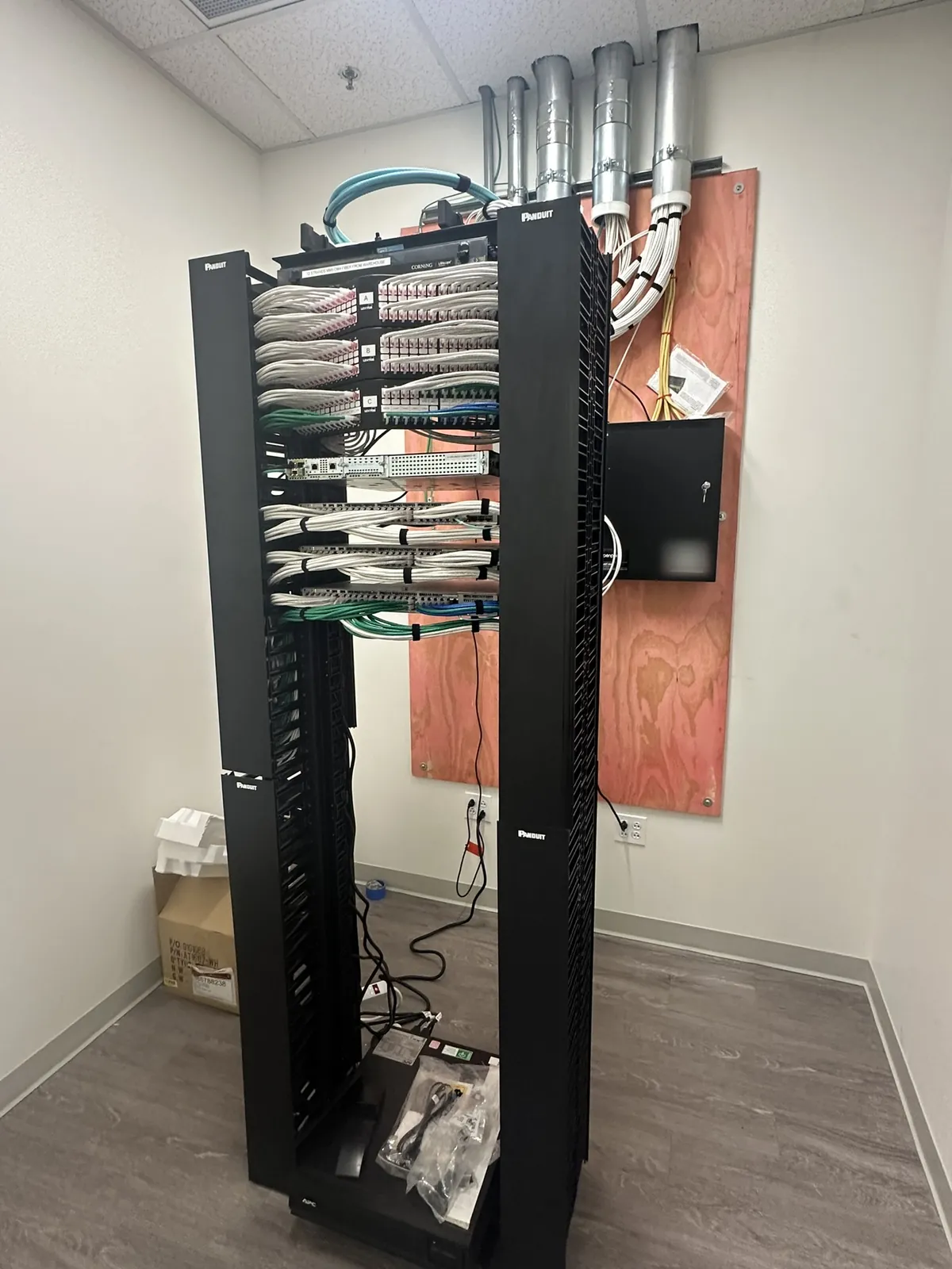 Freestanding two-post rack with patch panels beside a plywood backboard at a Data Pro Communications project in Orlando, FL